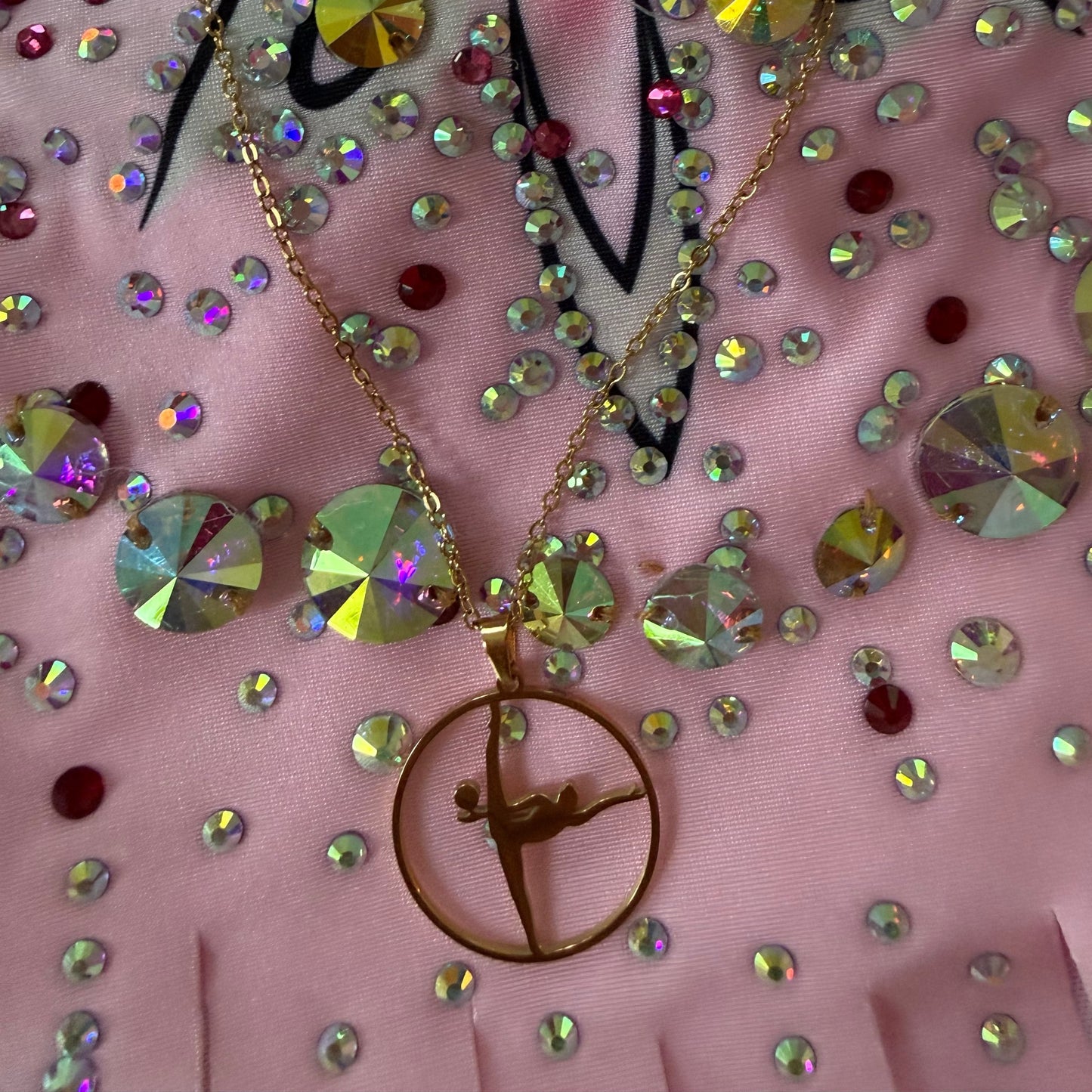 Necklace with a gold pendant on a pink fabric background with rhinestones