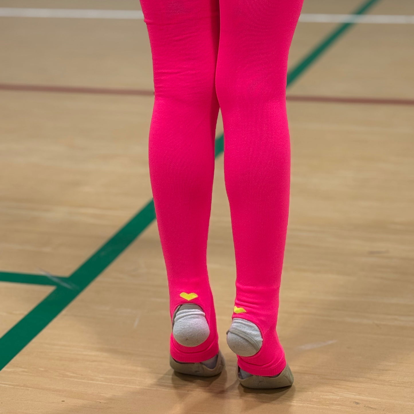 Gymnast wearing bright pink leg warmers and toe shoes on a wooden floor.