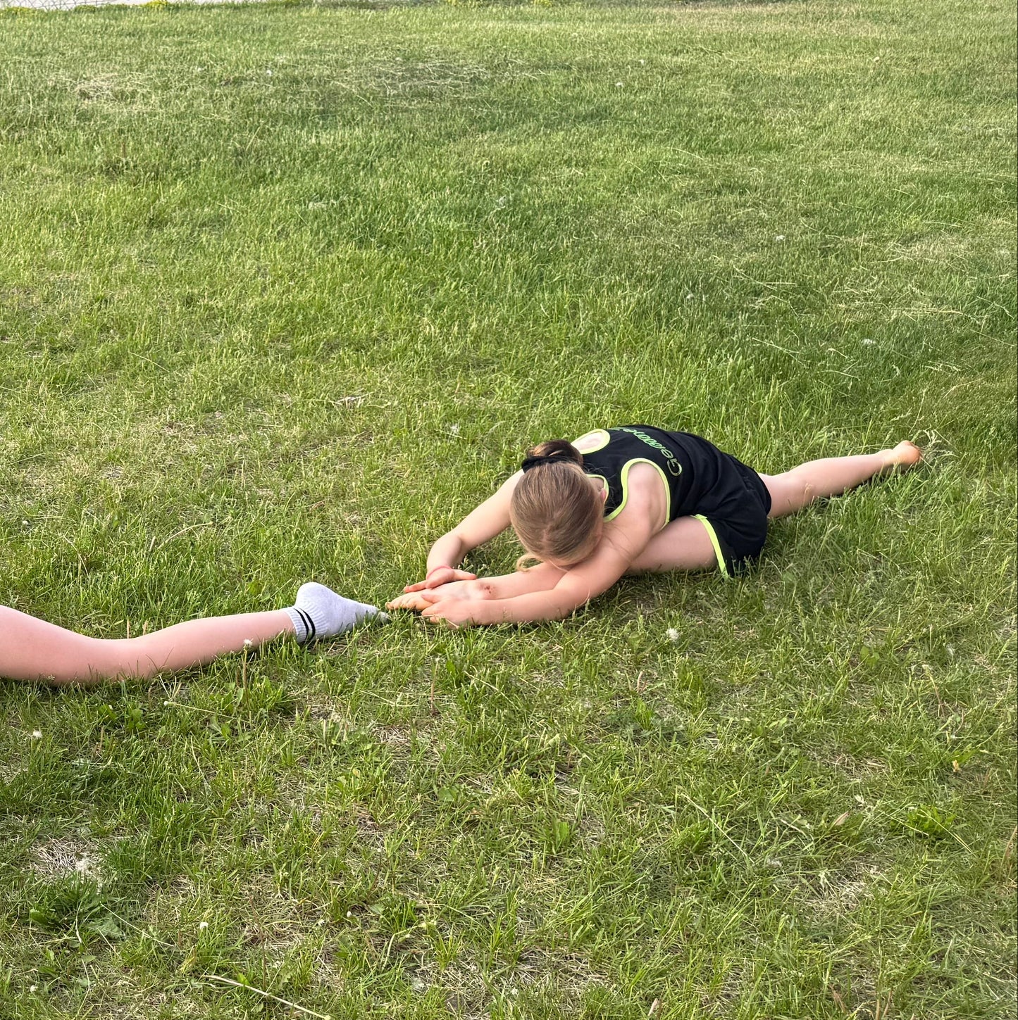 Gymnast in black Gemmez outfits stretching on a grassy field.