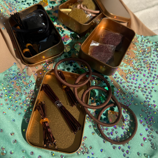 Collection of hair accessories including hair ties and clips in small metallic containers on a leotard glittery surface.