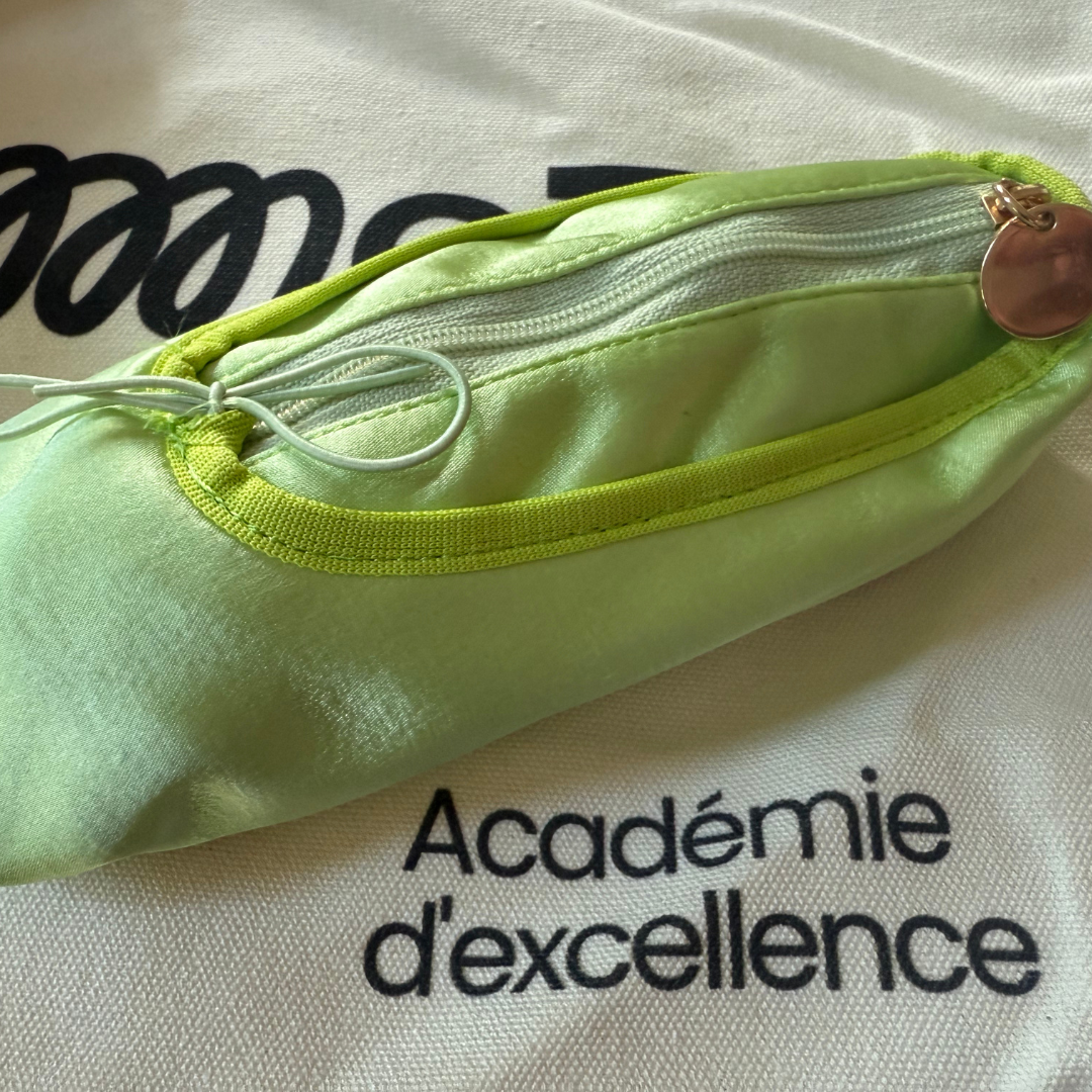 Light green pouch with a zipper on a gemmez bag background with 'Academie d'excellence' text.