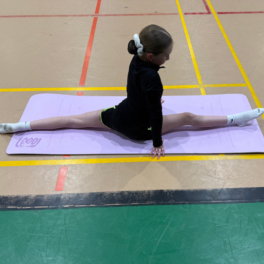 Gymnast performing a split on a Gemmez branded mat in a gymnasium