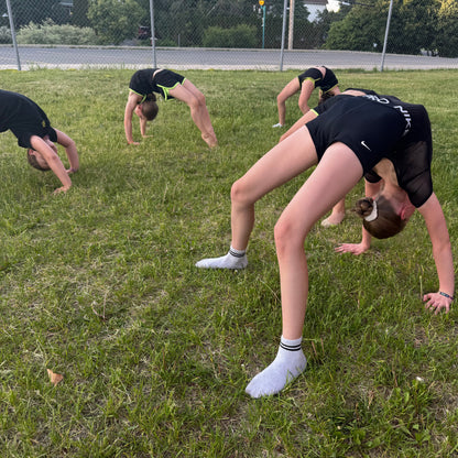 Group of gymnasts performing a bridge position on a grassy field