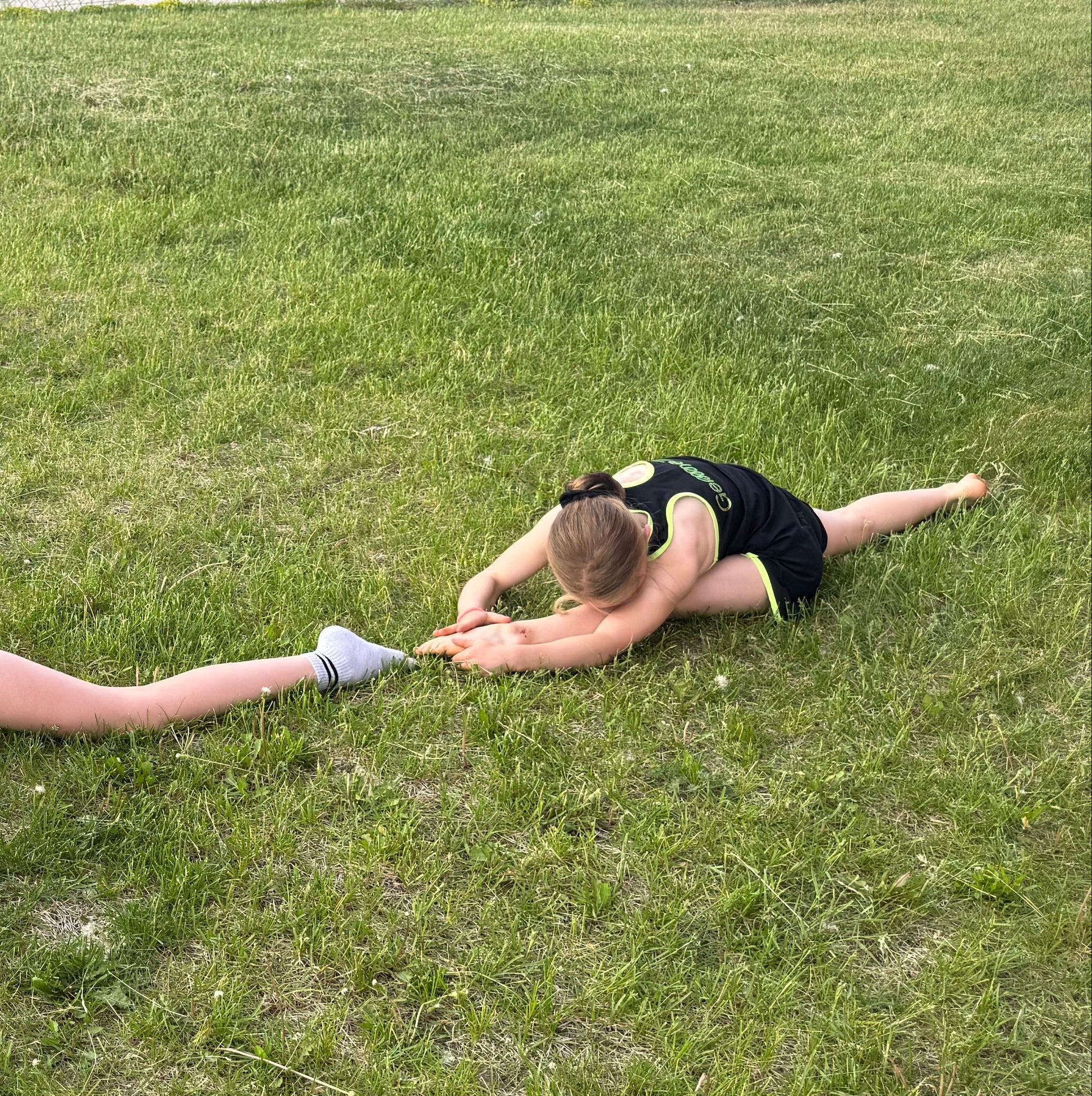Gymnast in black Gemmez outfits stretching on a grassy field.