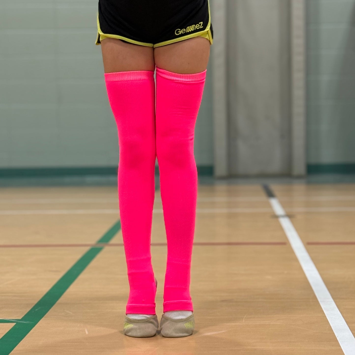 Gymnast wearing neon pink knee-high leg warmers in a gymnasium