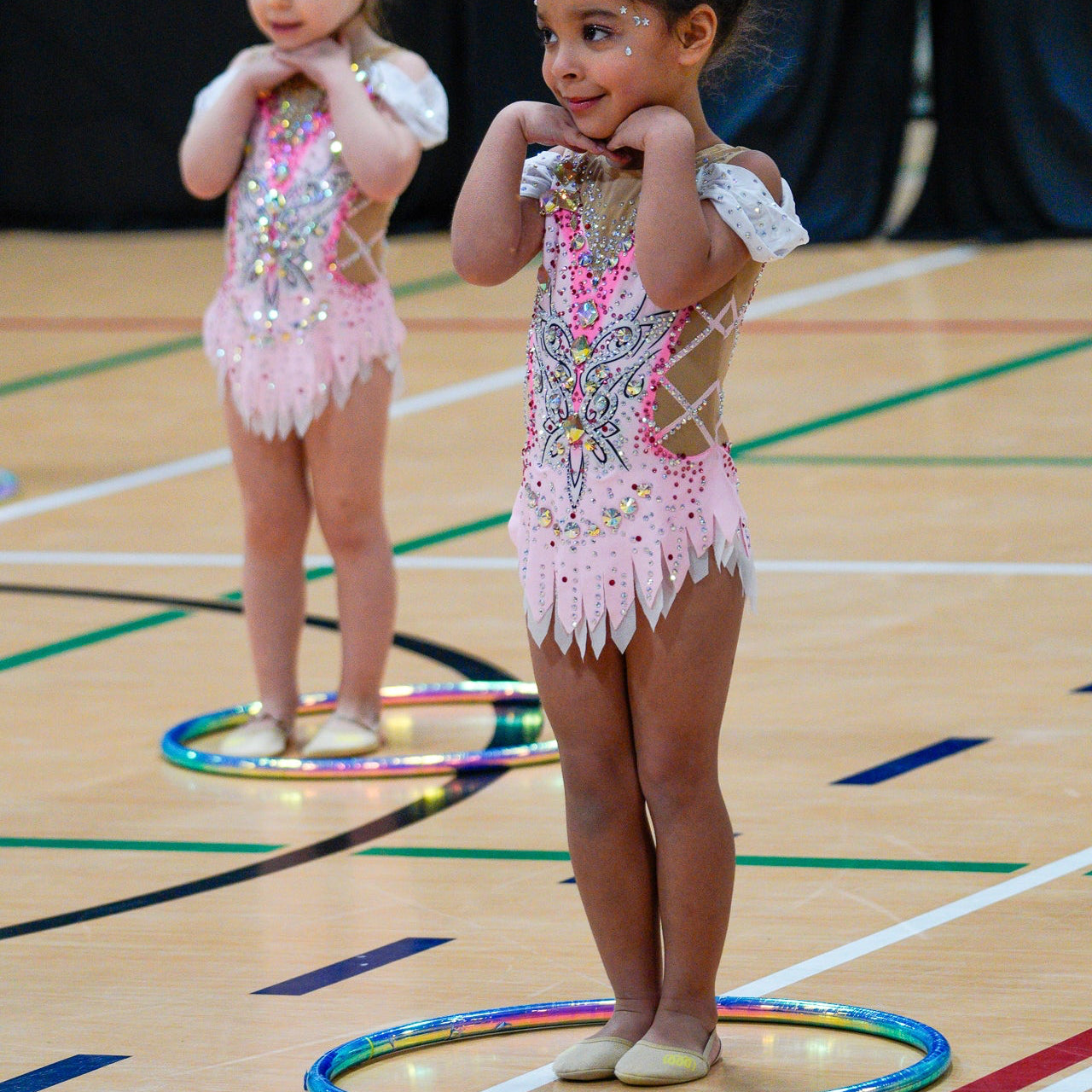 Two young gymnasts n pink leotards with sequins standing in hoops posing for a show.