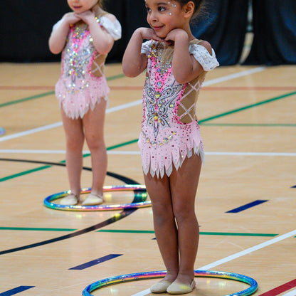 Two young gymnasts n pink leotards with sequins standing in hoops posing for a show.