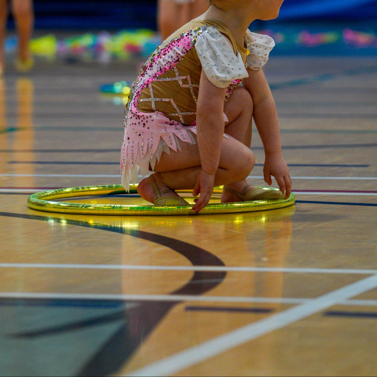 Young gymnast in a pink leotard sitting inside a yellow wrapped hoop