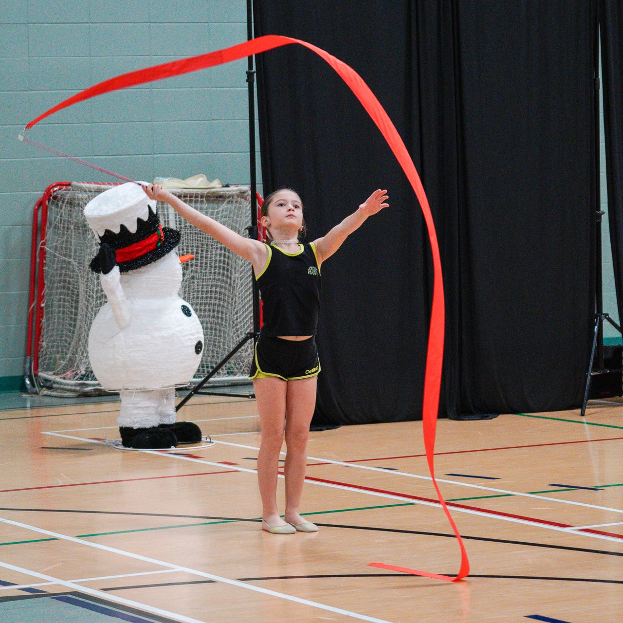 Young gymnast working rotations with red rayon ribbon dressed in gemmez branded rhinestones set.