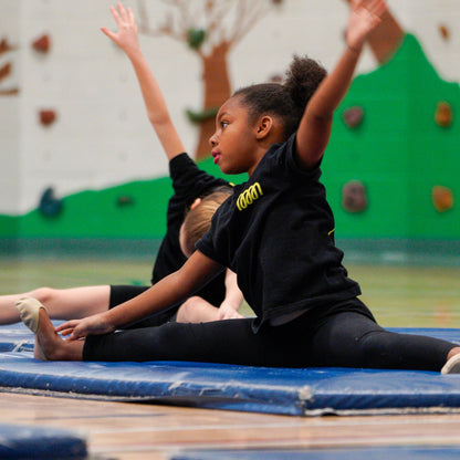 Two young gymnasts practicing split on a blue mat.