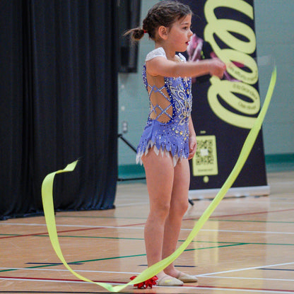 Young rhythmic gymnast in purple leotard showcasing green ribbon