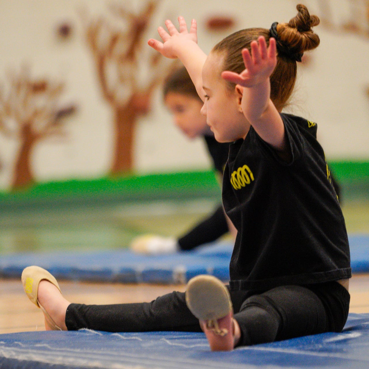 Young rhythmic gymnast in split position wearing t shirt and toe shoes of Gemmez with green swirls