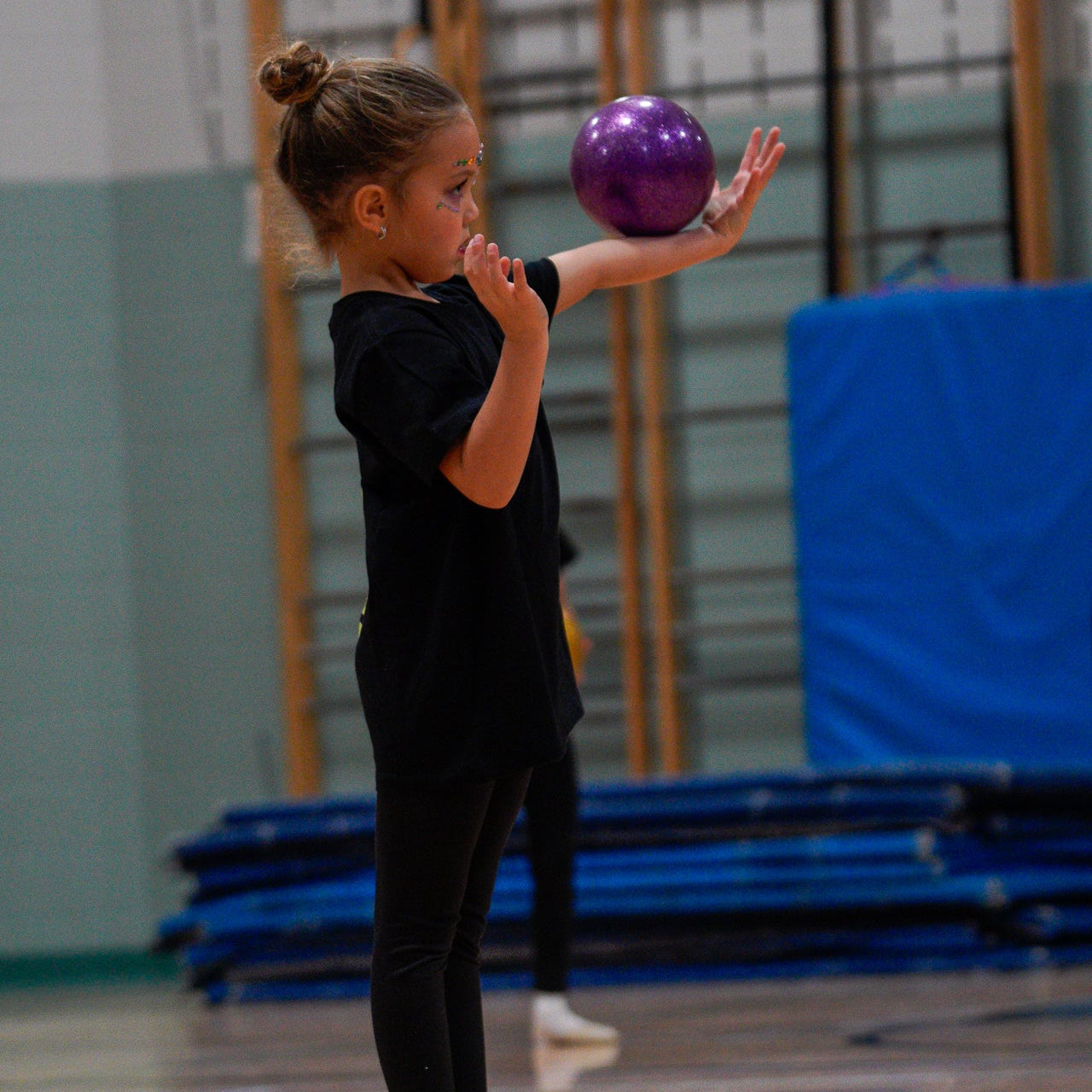 Young rhythmic gymnast rolling purple ball on her arm