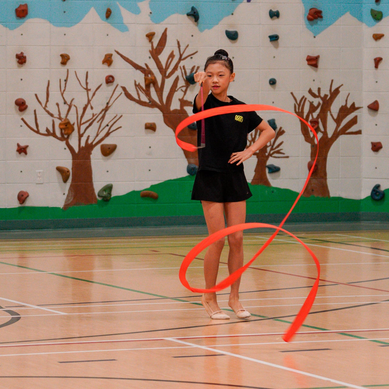 gymnast creating spirals with red rayon ribbon wearing the Gemmez brand t shirt