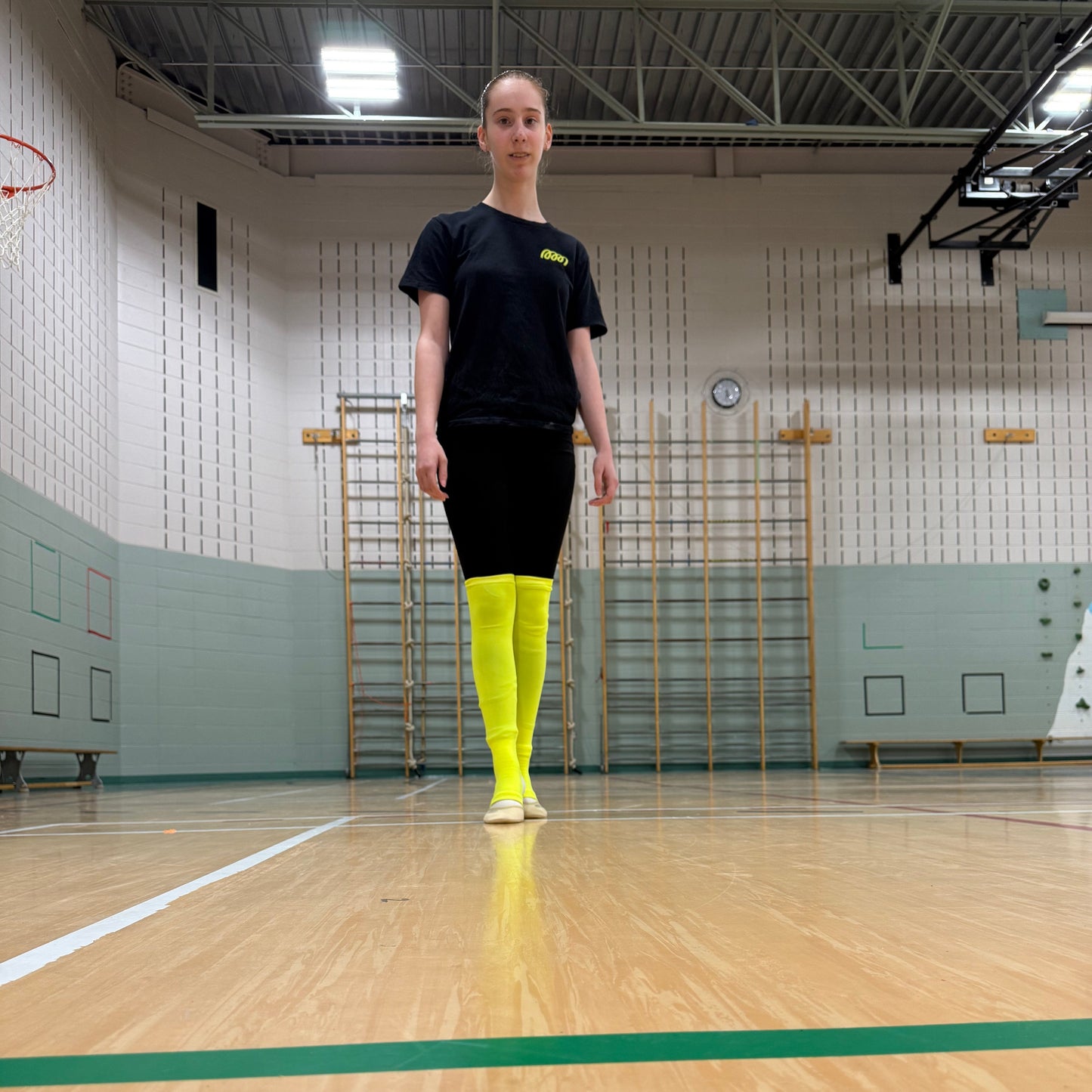 Gymnasts wearing a Gemmez black outfit with neon yellow leg warmers on a basketball court