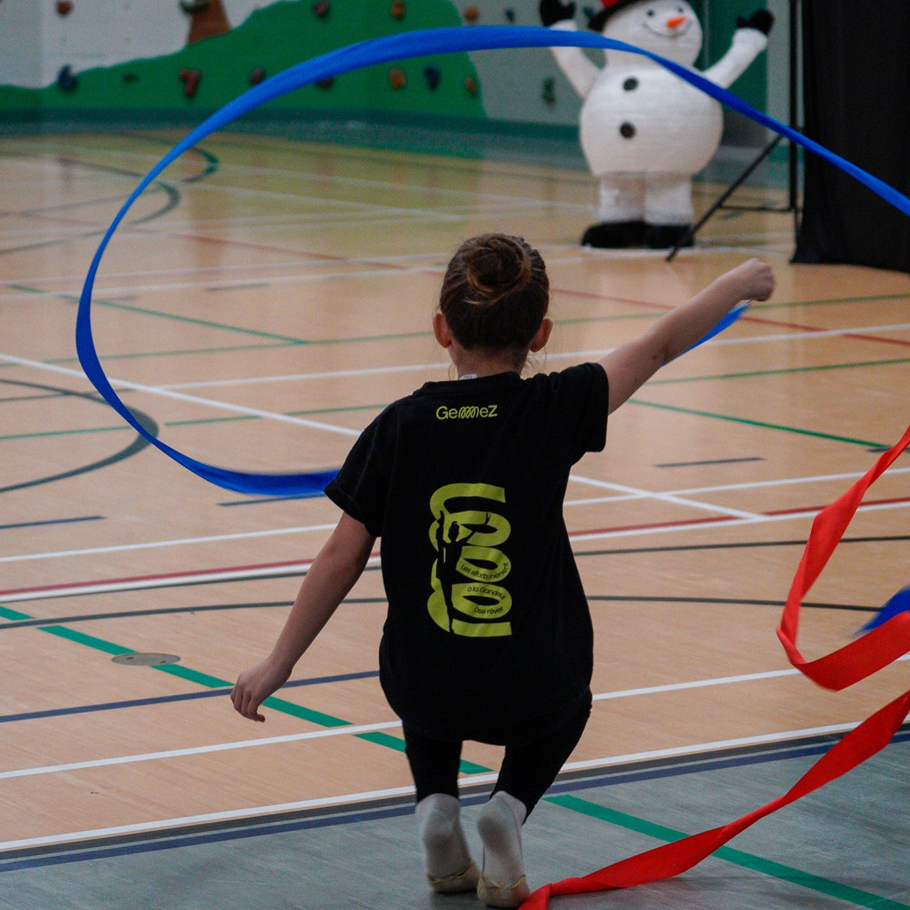 young gymnast rotating blue rayon ribbon in a duct walk position