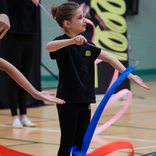 young gymnast working spirals with blue rayon ribbon wearing the Gemmez brand t short and leggings.